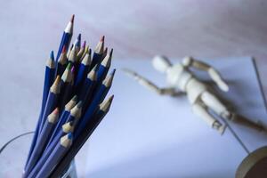 Colored pencils, empty paper and dummy for drawing on the table. photo