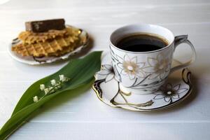 Lily of the valley, a cup of coffee and dessert on a white wooden table. photo