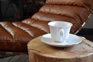 Porcelain cup on wooden coffee table near leather chair photo