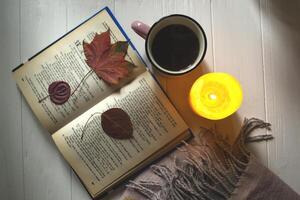 A cup of tea near book and woolen blanket with decoration by fallen leaves. Cozy autumn. photo