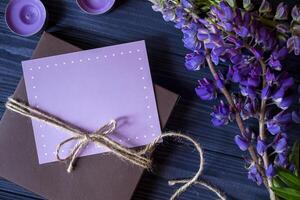 Gift box with greeting card and bouquet of lupins on a dark blue wooden background. photo