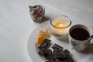 A candle, cup of coffee and black chocolate on the white plate. photo
