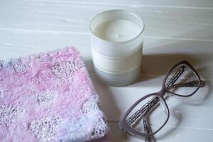 The closed pink notepad, white candle and glasses on a white wooden table. Work place still life. photo