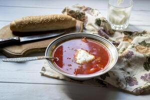 Red soup, bread and sour cream on a white wooden table. Borscht - a traditional dish of Russian cuisine. photo