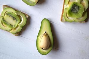 The sandwiches with avocado and kiwi on a white wooden background. photo