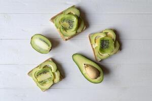 The sandwiches with avocado and kiwi on a white wooden background. photo