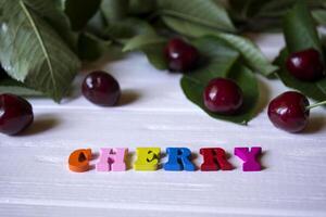 The branch with ripe cherries and multicolor letters on a white wooden table. photo