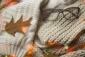 Eyeglasses, notepad and autumn leaf on the knitted plaid. Winter flat lay. Hygge style. photo