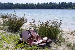 Female shoes and pink glasses on the coast of blue lake. photo