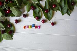 The branch with ripe cherries and multicolor letters on a white wooden table. photo