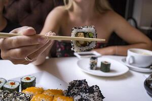 Woman is holding sushi roll in bamboo sticks. photo