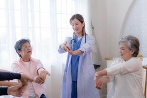 Portrait of elderly smiling Asian woman and people aerobics in nursery house. Seniors are moving their body arms and shoulders for a healthy life. retired people activities group concept. photo