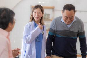 Asian young nurse support senior older man walk with walker. Beautiful nurse help and take care. elderly mature grandpa patient doing physical therapy with a group of senior friends in hospital. photo