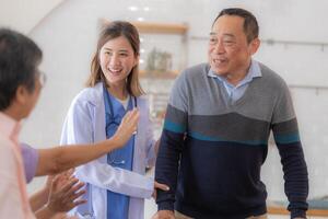 Asian young nurse support senior older man walk with walker. Beautiful nurse help and take care. elderly mature grandpa patient doing physical therapy with a group of senior friends in hospital. photo