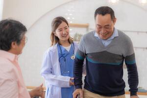 Asian young nurse support senior older man walk with walker. Beautiful nurse help and take care. elderly mature grandpa patient doing physical therapy with a group of senior friends in hospital. photo