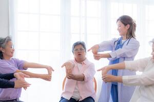 Portrait of elderly smiling Asian woman and people aerobics in nursery house. Seniors are moving their body arms and shoulders for a healthy life. retired people activities group concept. photo