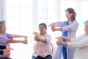 Portrait of elderly smiling Asian woman and people aerobics in nursery house. Seniors are moving their body arms and shoulders for a healthy life. retired people activities group concept. photo