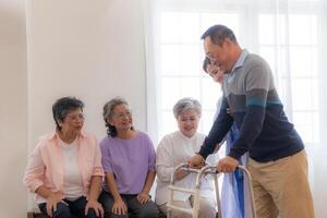 Asian young nurse support senior older man walk with walker. Beautiful nurse help and take care. elderly mature grandpa patient doing physical therapy with a group of senior friends in hospital. photo