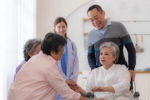 Asian young nurse support couple senior older man and woman in a wheelchair. elderly mature and a group of senior friends living in the hospital. socializing of retired people. photo