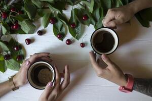 Female hands with coffee against a white wooden background, with ripe cherries. Top view. photo