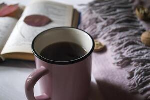 A cup of tea near book and woolen blanket with decoration by fallen leaves. Cozy autumn. photo