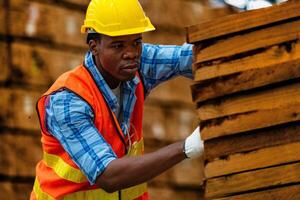 African worker carpenter wearing safety uniform and hard hat working and checking the quality of wooden products at workshop manufacturing. man and woman workers wood in dark warehouse industry. photo