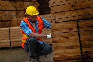 African worker carpenter wearing safety uniform and hard hat working and checking the quality of wooden products at workshop manufacturing. man and woman workers wood in dark warehouse industry. photo