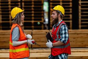 workers carpenter wearing safety uniform and hard hat working and checking the quality of wooden products at workshop manufacturing. man and woman workers wood in dark warehouse industry. photo