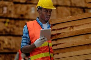 African worker carpenter wearing safety uniform and hard hat working and checking the quality of wooden products at workshop manufacturing. man and woman workers wood in dark warehouse industry. photo