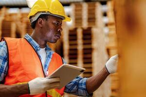 African worker carpenter wearing safety uniform and hard hat working and checking the quality of wooden products at workshop manufacturing. man and woman workers wood in dark warehouse industry. photo