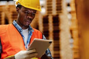 African worker carpenter wearing safety uniform and hard hat working and checking the quality of wooden products at workshop manufacturing. man and woman workers wood in dark warehouse industry. photo