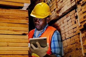 African worker carpenter wearing safety uniform and hard hat working and checking the quality of wooden products at workshop manufacturing. man and woman workers wood in dark warehouse industry. photo