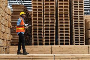 African workers man engineering walking and inspecting with working suite dress and hand glove in timber wood warehouse. Concept of smart industry worker operating. Wood factories produce wood palate. photo