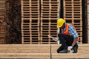 African workers man engineering walking and inspecting with working suite dress and hand glove in timber wood warehouse. Concept of smart industry worker operating. Wood factories produce wood palate. photo