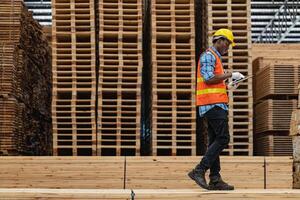 African workers man engineering walking and inspecting with working suite dress and hand glove in timber wood warehouse. Concept of smart industry worker operating. Wood factories produce wood palate. photo