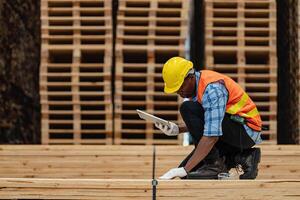 African workers man engineering walking and inspecting with working suite dress and hand glove in timber wood warehouse. Concept of smart industry worker operating. Wood factories produce wood palate. photo