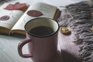 A cup of tea near book and woolen blanket with decoration by fallen leaves. Cozy autumn. photo