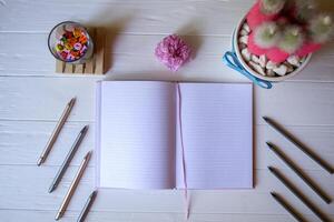 A notepad with pen, pink cactus, crumpled sheet of paper and multicolored letters on a white wooden desktop. photo