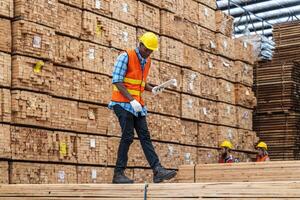 African workers man engineering walking and inspecting with working suite dress and hand glove in timber wood warehouse. Concept of smart industry worker operating. Wood factories produce wood palate. photo