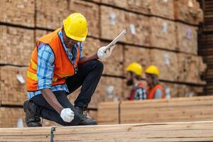 African workers man engineering walking and inspecting with working suite dress and hand glove in timber wood warehouse. Concept of smart industry worker operating. Wood factories produce wood palate. photo