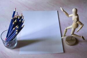 Colored pencils, empty paper and dummy for drawing on the table. photo