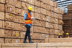 African workers man engineering walking and inspecting with working suite dress and hand glove in timber wood warehouse. Concept of smart industry worker operating. Wood factories produce wood palate. photo