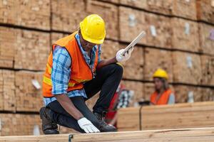 African workers man engineering walking and inspecting with working suite dress and hand glove in timber wood warehouse. Concept of smart industry worker operating. Wood factories produce wood palate. photo