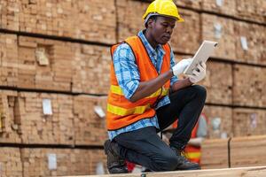 African workers man engineering walking and inspecting with working suite dress and hand glove in timber wood warehouse. Concept of smart industry worker operating. Wood factories produce wood palate. photo