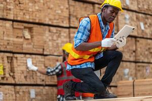 African workers man engineering walking and inspecting with working suite dress and hand glove in timber wood warehouse. Concept of smart industry worker operating. Wood factories produce wood palate. photo