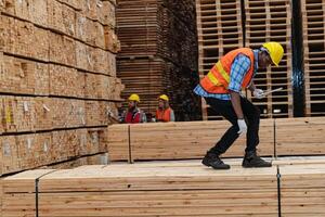 African workers man engineering walking and inspecting with working suite dress and hand glove in timber wood warehouse. Concept of smart industry worker operating. Wood factories produce wood palate. photo