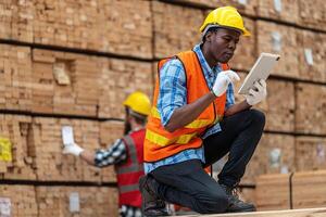 African workers man engineering walking and inspecting with working suite dress and hand glove in timber wood warehouse. Concept of smart industry worker operating. Wood factories produce wood palate. photo