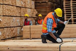 African workers man engineering walking and inspecting with working suite dress and hand glove in timber wood warehouse. Concept of smart industry worker operating. Wood factories produce wood palate. photo