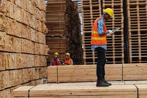 African workers man engineering walking and inspecting with working suite dress and hand glove in timber wood warehouse. Concept of smart industry worker operating. Wood factories produce wood palate. photo