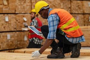 African workers man engineering walking and inspecting with working suite dress and hand glove in timber wood warehouse. Concept of smart industry worker operating. Wood factories produce wood palate. photo